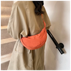 Bright orange nylon crescent bag worn crossbody over a classic khaki trench coat