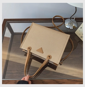 Detail of woven straw tote bag featuring brown leather straps and a triangle emblem