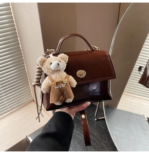 Detail view of dark brown oil wax leather handbag with golden lock and bear charm