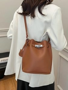 Brown leather bucket bag with silver twist lock shown on model in white blazer