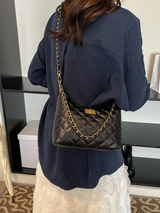 Sac bandoulière matelassé noir avec chaîne dorée porté par un mannequin vue de dos