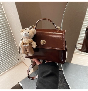 Detail of dark brown patent leather handbag featuring a gold buckle and bear plush charm