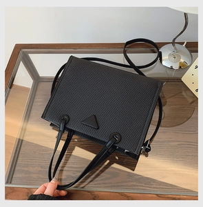 Detail of black woven texture tote bag with triangular patch on a stylish glass table