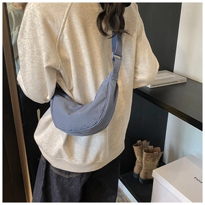 Detailed close-up of a blue nylon crescent bag worn crossbody by a model in casual style