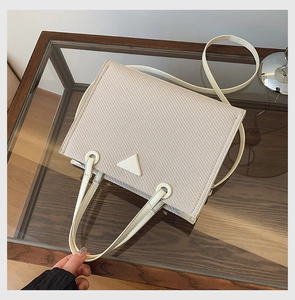 Detailed view of cream woven texture handbag with triangular emblem and dual handles