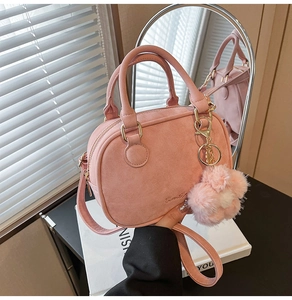 Detailed mirror view of a pink suede barrel bag with plush flower charm and gold hardware