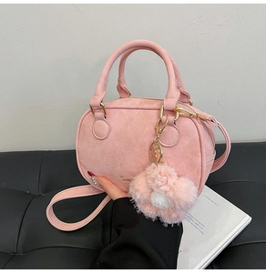 Pink suede handbag with plush flower charm and gold hardware on a textured black surface