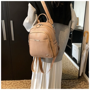 Detail of the camel PU leather backpack featuring metal ring zippers and textured finish
