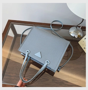 Detail view of light blue textured fabric handbag with top handles and shoulder strap