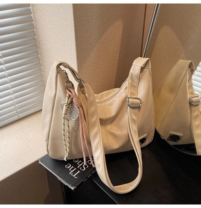 Detail of a beige hobo bag showing faux leather texture and silver racquet pendant