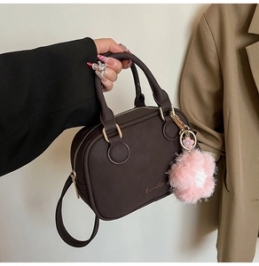 Detail of dark brown leather Boston bag with gold ring handles and pink floral charm