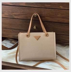 Detail of beige woven tote with brown leather handles and triangle logo patch