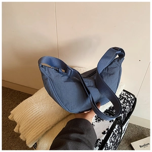 Blue nylon crescent bag with adjustable strap shown against a travel background