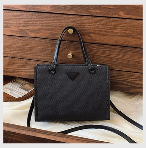 Detail view of black Saffiano textured tote bag on wooden chest with elegant silk drape
