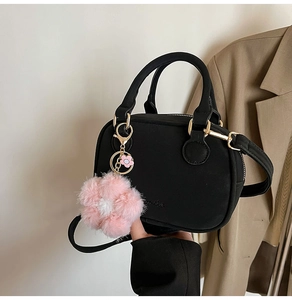 Detail of black satchel bag featuring a pink plush flower charm and gold hardware