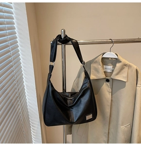 Detail of black leather hobo bag with silver buckle hanging next to a beige trench coat