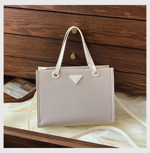 Detail of beige Saffiano leather tote bag with elegant triangle plaque on white silk