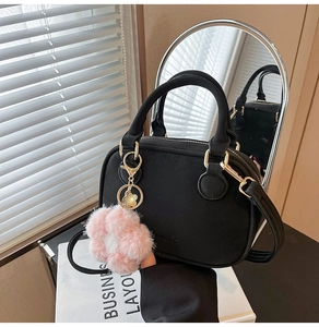 Detail of black textured handbag with golden hardware and pink plush flower charm