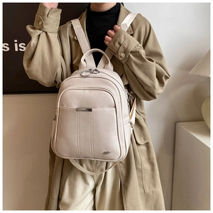 Detail view of off-white lychee texture leather backpack worn with chic trench coat