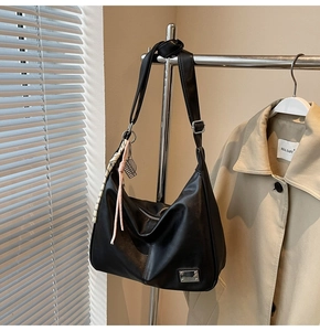Detail of black leather hobo bag featuring woven rope charm and silver brand plate