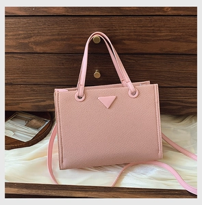 Detail of pink Saffiano leather tote bag featuring a triangle plaque and slim strap