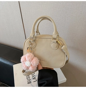 Detail of beige pillow bag with plush flower pendant and adjustable shoulder strap