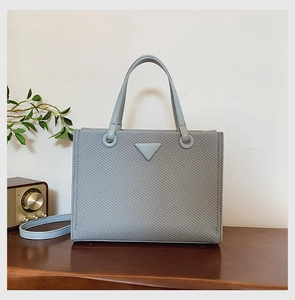 Detail of woven light blue tote bag with triangular logo and leather shoulder strap