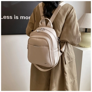 Detail of a beige pebbled leather backpack with silver zippers and multi-layer storage