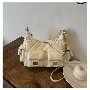 Detail of cream quilted crescent bag with gold twist locks and chain strap on wood table