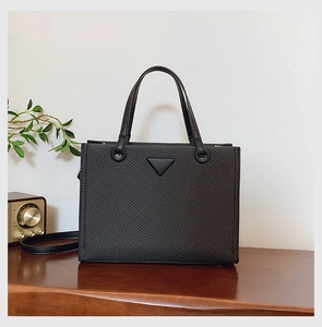 Close-up of black woven tote bag with triangular logo on a vintage wooden table