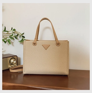 Detail of beige woven tote bag with triangular plaque and brown leather handles