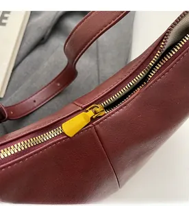 Close-up of smooth gold metal zipper and leather texture on dark red shoulder bag
