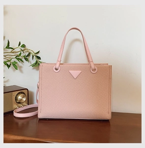 Detailed close-up of pink woven texture handbag with metallic triangle logo and gold hardware