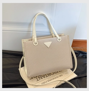 Detailed top view of beige woven tote bag with triangular metal plate and shoulder strap