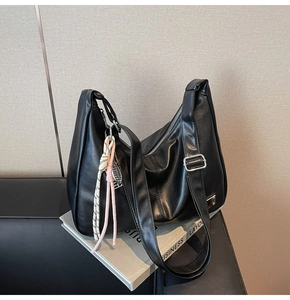 Detail of a black half-moon shoulder bag with an adjustable strap and pink woven charm
