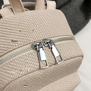 Detail of silver metal double zippers and twill textured fabric on mini beige backpack