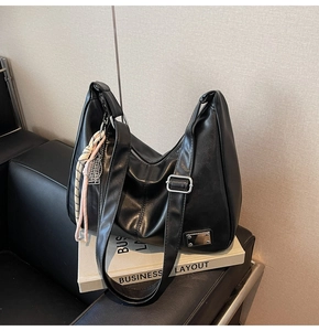 Detail of black leather hobo bag with pink woven charm on a classic leather chair