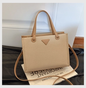 Close-up of beige woven tote bag with camel leather handles and triangular detail