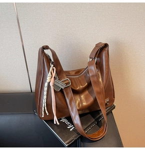 Detail of vintage brown PU leather hobo bag with woven knots and metal charm pendant