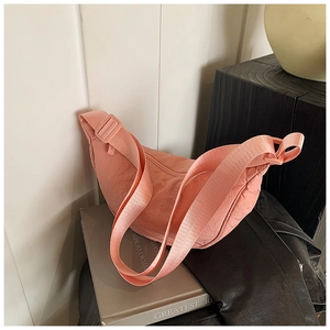 Detail of pink nylon crescent bag with adjustable strap on a book and leather jacket