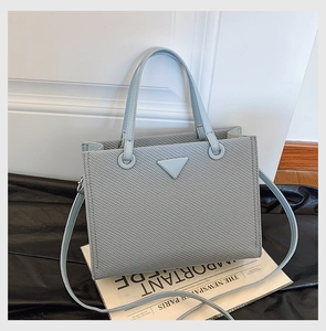 Detail of light blue-grey tote bag showing textured crosshatch leather and triangle hardware