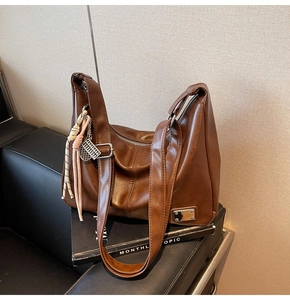 Close-up of brown textured leather tote with silver zipper and colorful woven charm