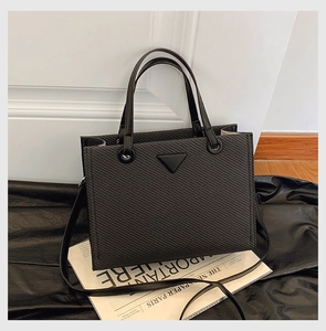 Detail view of black woven tote bag with iconic triangle logo and dual shoulder straps