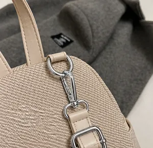 Detail showing the silver metal hook and beige woven fabric texture of the mini backpack