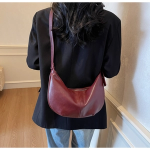 Model wearing a deep burgundy half-moon crossbody bag in a minimalist indoor setting