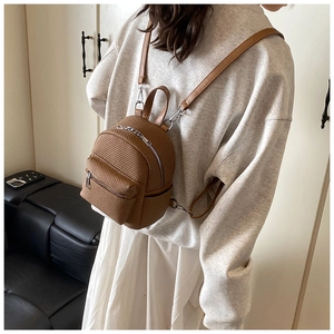 Detail of brown woven mini backpack featuring silver zippers and slim leather straps