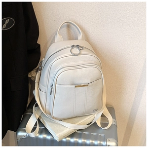 Close-up of a white lychee grain leather mini backpack placed on a silver suitcase