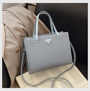 Light blue woven tote bag with triangular metal logo detail on a classic book