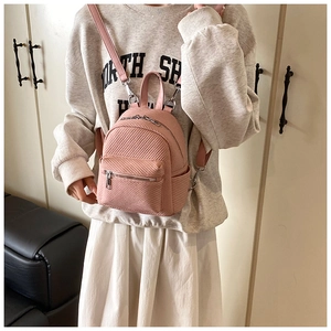 Pink mini backpack detail showing twill texture and slim straps on model in room