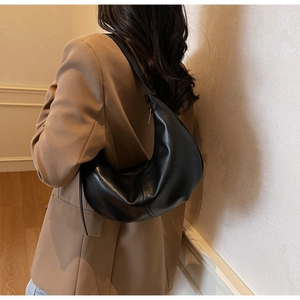 Chic black leather hobo bag with a sleek crescent shape shown on a model's shoulder
